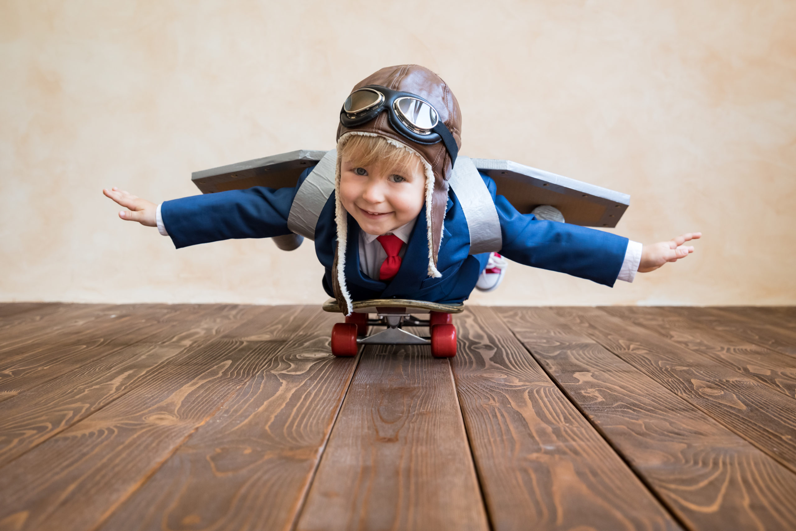 Portrait of young businessman with toy paper wings. Happy child playing at home. Kid having fun. Success, creative and start up concept